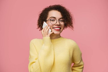 Neşeli genç bir kadın, canlı pembe bir arka plana gülümserken akıllı telefonuyla konuşuyor..