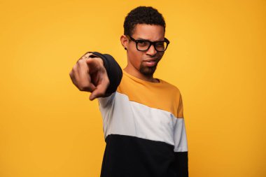 Şık giyinmiş gözlüklü genç bir adam, enerjik sarı bir arka plana karşı kameraya emin bir şekilde bakıyor. Görüntü güven, odaklanma ve canlı bir kişilik aktarır..