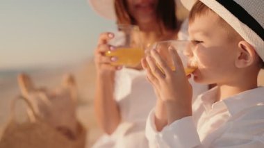 Anne ve oğlu güneşli bir sahilde serinletici bir içkinin tadını çıkarıyorlar. Rahatlama ve bağlantı odaklı mükemmel bir aile tatilinin özünü yakalamak..