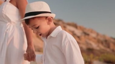 Bir anne ve küçük oğlu güzel bir sahil boyunca el ele yürüyorlar. İkisi de beyaz giyiyorlar ve mutlu görünüyorlar. Güneş parlıyor ve kum altın..