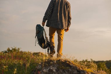 Gün batımında, sırtında sırt çantasıyla resimli bir tepede yürüyüş yapan bir adam..