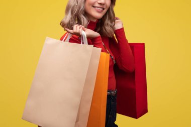 Neşeli bir kadın, canlı sarı bir arka plana karşı renkli alışveriş torbaları sergiliyor, alışveriş deneyiminden duyduğu haz ve memnuniyeti dile getiriyor. Mükemmel bir şekilde eğlence, ticaret ve eğlence kavramını yakalıyor.