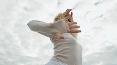 Düşük açılı bir görüntü, güzel, esnek bir kadını, huzurlu bir gökyüzü ile dans ederken yakalar..