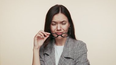 Şık takım elbiseli kendine güvenen genç bir kadın küstah bir ifadeyle gözlüklerini çıkarıyor ve durumu inceliyor..