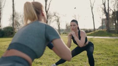 İki atletik kadın, dışarıda çömelirken, parkta spor yaparken karşı karşıya gelir..