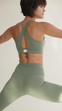 Yetişkin bir esmerin yoga kıyafeti giymiş, vücut bulmuş ve dengeli bir şekilde savaşçı pozu vermesini yakından izliyoruz..