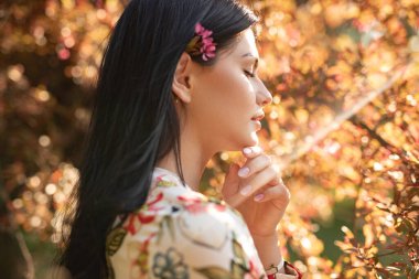 Açık havada, sarı-turuncu sonbahar yaprakları ve ılık güneş ışığıyla süslenmiş bir kadının huzurlu bir yan portresi..