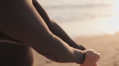 Bir sörfçü sabahın erken saatlerinde sörf yapmaya hazırlanıyor. Dalgalar dalgalanırken kumlu bir sahilde dalgıç kıyafetini giyiyor..