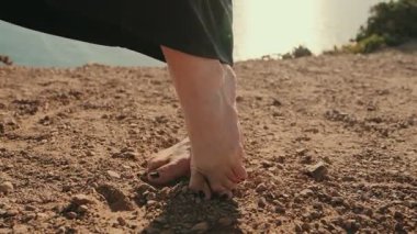 Okyanusun yakınındaki kumlu zeminde dans eden çıplak ayaklı kadının yakın çekimi ayaklarıyla sanatsal hareketler yaratıyor..