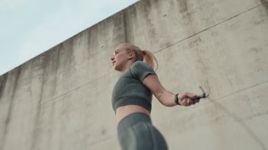 Beton arka planda ip atlayan atletik bir kadının düşük açılı görüntüsü, hareket yakalama ve açık havada spor eğitimi..