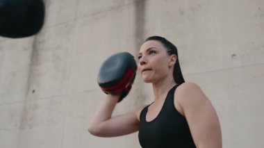 İki atletik kadın açık havada boks antrenmanı yapıyor. Odaklanmış kişisel antrenörle pedleri kullanarak yumruk antrenmanı yapıyorlar..