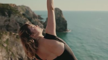 Tanınmayan bir kadın, güzel bir sahil uçurumuna ve okyanus zeminine karşı zarif bir şekilde dans ediyor..