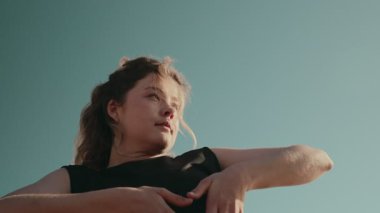 Siyah elbiseli genç bir kadının yakın çekim görüntüsü açık gökyüzüne karşı anlamlı bir pozla dans etmekten zevk alıyor.