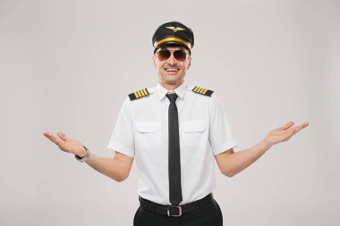 Profesyonel üniformalı neşeli bir uçak kaptanı omuz silkip, dostluk ve kendine güveni ifade ederek, misafirperver ve rahat bir ortam yaratıyor..