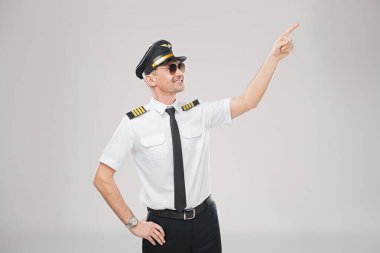 Beyaz üniformalı, kravatlı ve Kaptan şapkalı profesyonel bir erkek pilot tarafsız bir arkaplana doğru bakıyor..