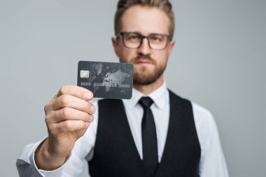 Resmi giyinmiş profesyonel bir adam kredi kartı sunuyor, finansal hizmetleri, iş kavramlarını ve modern finansal ekosistemdeki güvenliği simgeliyor..