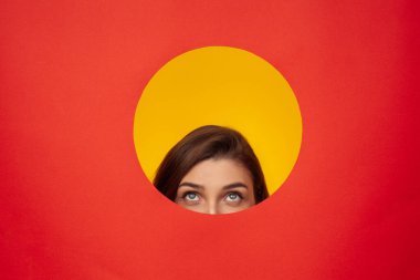 Yaratıcı ve oyuncu bir portre. Renkli kırmızı ve sarı bir arkaplandan bakan bir kadın. Çarpıcı renkler ve geometrik kompozisyon ile merak ve yenilikçi düşünceyi sembolize eder.