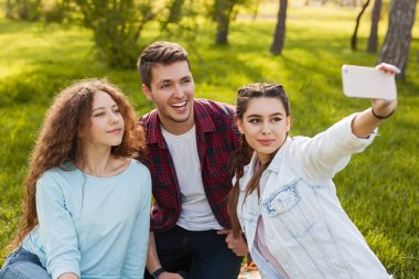 Üç arkadaş güneşli bir parkta birlikte vakit geçiriyorlar, bir selfie ile anıları yakalıyorlar..