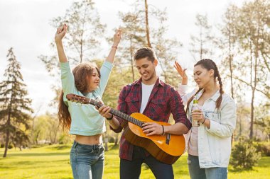 Üç arkadaş parkta güneşli bir günün tadını çıkarıyorlar, gitar çalıp, şarkı söyleyip, dans ediyorlar, doğal ve rahat bir ortamda neşe ve beraberlik sergiliyorlar..