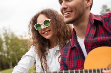 İki arkadaş açık havada güneşli bir günün tadını çıkarıyor, gülümsüyor ve gitar çalıyor, arkadaşlığı ve neşeyi kucaklıyor. Doğal ortamda mutluluk ve rahatlama dolu müzikal ve canlı bir atmosfer gösteriliyor..