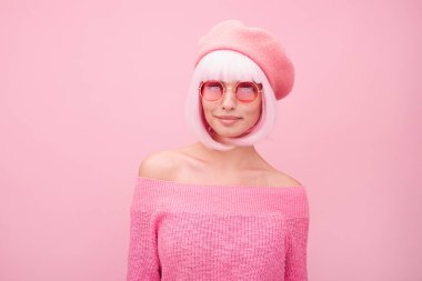 Pembe bir süveter, güneş gözlüğü ve bere takan şık bir kadının portresi. Pembe bir arka fonun önünde. Koordineli monoton düzeninde stili ve yaratıcılığı simgeliyor..