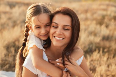 Güler yüzlü bir anne ve kızın, güneşli bir günde kırsal bir ortamda birbirine sarılıp sevgisini, bağlantısını ve doğal huzurunu sergilediği güzel, samimi bir an..