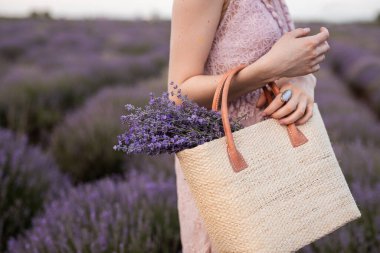 Lavanta tarlasında elinde sepet ve taze lavanta tutan bir kadının kısmi görüntüsü. Bu dingin sahne sükuneti, doğayı ve çiçek açan güzelliği çağrıştırıyor..