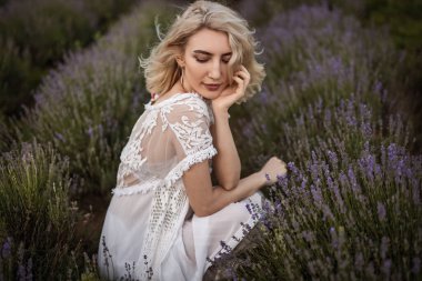 Zarif dantelli beyaz elbiseli sakin bir kadın zarif bir şekilde etrafı çiçeklerle çevrili, açık havada huzur ve doğal güzellik yayıyor..