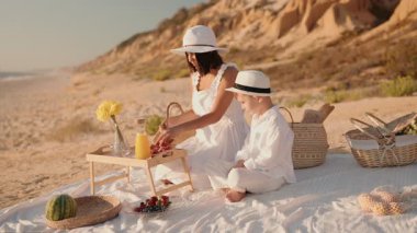 Bir anne ve oğlu gün batımında plajda rahat bir pikniğin tadını çıkarırlar. İkisi de bembeyaz giyinmiş ve manzara huzur verici ve iç açıcı..