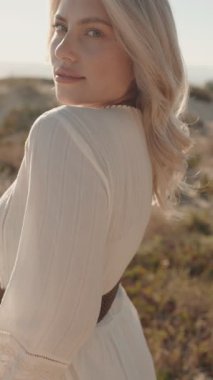 Sarışın, beyaz elbiseli, güzel bir genç kadın kumsaldaki temiz havanın tadını çıkarıyor.