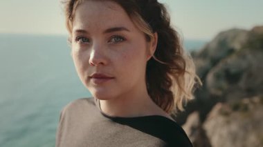 Okyanus kayalıklarının yanında duran genç bir kadının portresi, doğal bir geçmişi olan düşünceli ve huzurlu görünüyor..