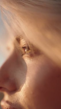 Rüzgarda savrulan sarı saçlı bir kadının yavaş çekim videosu. Güneş yüzüne vuruyor ve gözleri kapalı..