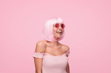 Renkli pembe bir arka planda moda güneş gözlüğü takan, şık, pembe kısa saçlı neşeli bir genç kadının portresi. Modern ve oyuncu ifade, yaratıcı moda ve yaşam tarzı temaları için mükemmel..