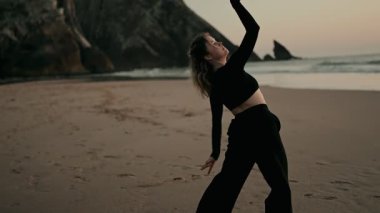 Gün batımında bir kumsalda zarif bir şekilde dans eden bir kadının doğal çevreyle bir özgürlük ve güzellik anı yakaladığı huzurlu bir sahne..