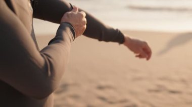 Dalgıç kıyafeti giyip sahilde sörf yapmaya hazırlanan bir sörfçünün yakın çekimi. Güneşin altın ışığı sahneyi aydınlatıyor, sakin ve huzurlu bir atmosfer yaratıyor..