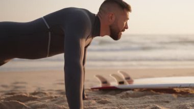 Bir sörfçü dalgalara çarpmadan önce ısınmak için plajda şınav çeker. Fitness, egzersiz ve hazırlık sörfçüler için gereklidir..