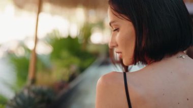 Kısa saçlı, kırmızı tırnak cilası olan esmer bir kadın bekliyor ve düşüncelere dalıyor. Sonra saçlarını kulağının arkasına saklar ve yukarı bakar..