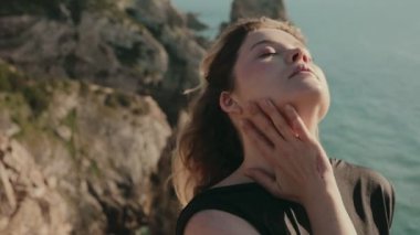 Sahil kenarındaki bir uçurumun kenarında huzur ve farkındalık hisseden bir kadının huzurlu görüntüsü. Doğal bir manzarada barışçıl duygular yakalamak.