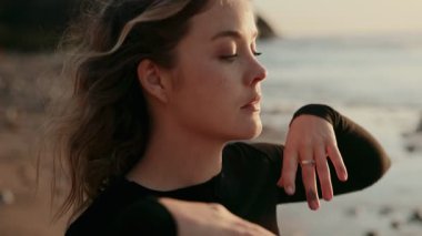 Gün batımında sakin bir plajda gözleri kapalı poz veren zarif bir dansçının portresi zarafet ve sükunet sergiliyor..