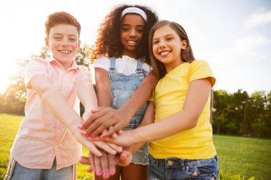 Çimenli bir alanda güneşli bir günde birlik ve dostluk içinde el ele tutuşan üç neşeli çocuktan oluşan bir grup. Beraberliği, takım çalışmasını ve çocukluk sevincini sembolize ediyorlar..