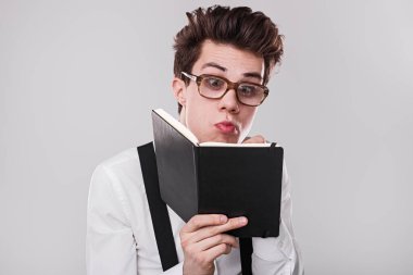 Gözlük ve pantolon askısı takan genç bir adam bir defter okumaya derinden odaklanır. Merakını ve bağlılığını ifade edişi bir anlık entelektüel dalgınlığı vurguluyor..