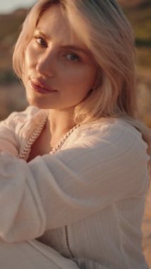 Gün batımının altın ışığı yüzünde parlarken kendinden emin genç kadın kameraya hafifçe gülümsüyor..