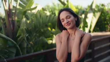 Genç bir kadın, tropikal bir tatilde gülümser ve dinlenir. Sıcak havanın ve yemyeşil havanın tadını çıkarır. Seyahat, rahatlama ve sağIık kavramları için mükemmel..