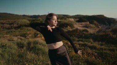 Moda kıyafetleri içinde genç bir bayan dansçı, özgürlüğünü ve zarafetini ifade eden doğa manzaralı bir ortamda güzel bir çağdaş dans sergiliyor..