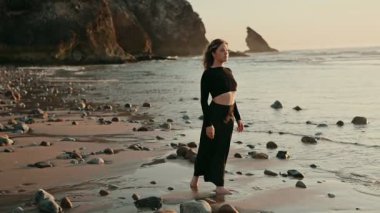 Genç bir kadın güzel bir sahilde duruyor, okyanusa bakıyor. Batan güneş, huzurlu ve düşünceli bir atmosfer sunarak ılık bir parıltı yayar..