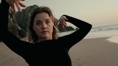 Gün batımında sakin bir plajda zarif bir şekilde dans eden bir kadın okyanusun yanında huzurlu ve anlamlı bir anı yakalar..