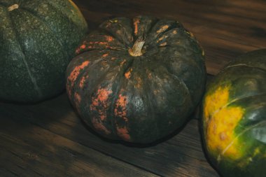 Tahta bir masanın üzerinde üç balkabağı sıralanmış. Cadılar Bayramı 'nda loş ışıkta acımasız bir fotoğraf. Cadılar Bayramı 'nda evi dekore etmek için balkabakları..