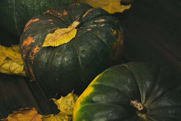 A gloomy photo with pumpkins and dim light. Pumpkins in the dark with autumn leaves on a wooden background. On the table are three pumpkins with leaves. autumn decorations.