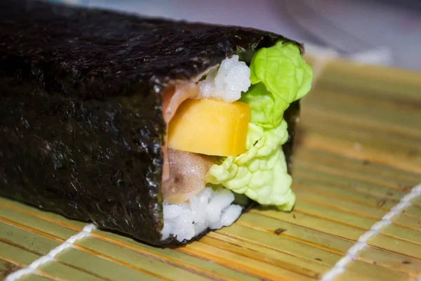 Sushi and fish are twisted but not cut. A long roll of sushi. Create roles. Twisted roll of nori up close.