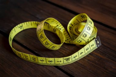 Modelin uzunluğunu ve hacmini ölçmek için terzi ölçer. Ölçüm bandı tahta bir tahtanın üzerinde. Masanın üzerinde sarı bir dikiş makinesi var..